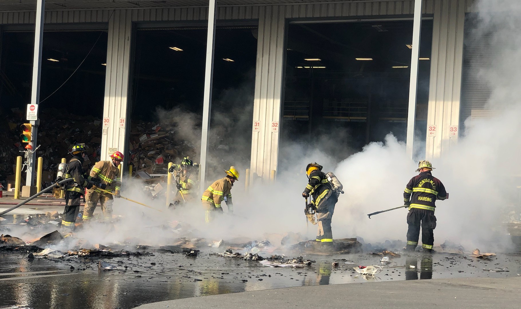 A group of firefighters stands around a large pile of debris